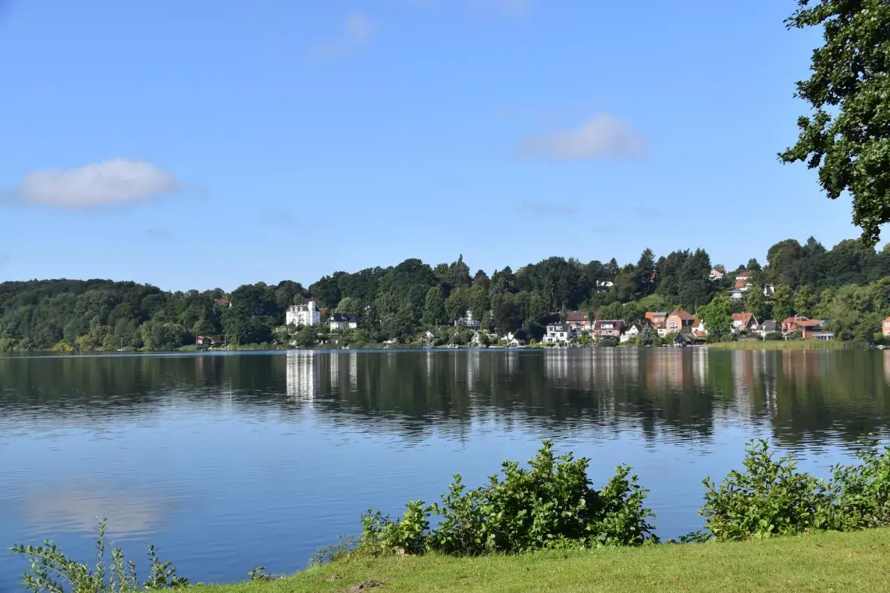 Blick auf die Ratzeburg Altstadt mit ihren Häusern, die sich an den grünen Hügel schmiegen, gespiegelt im ruhigen Wasser des Sees.