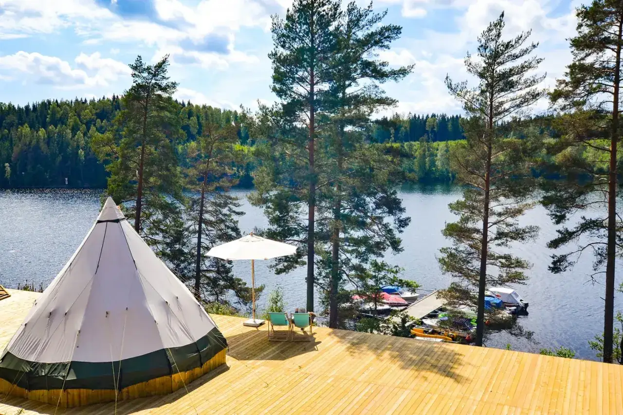 En stor tipi-tält på en träaltan vid en sjö, omgiven av skog. Perfekt för natur camping.