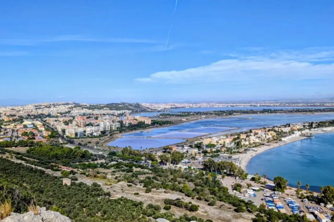 Vy över Cagliari, Sardinien, med saltbassänger, stad och kustlinje under en klarblå himmel.