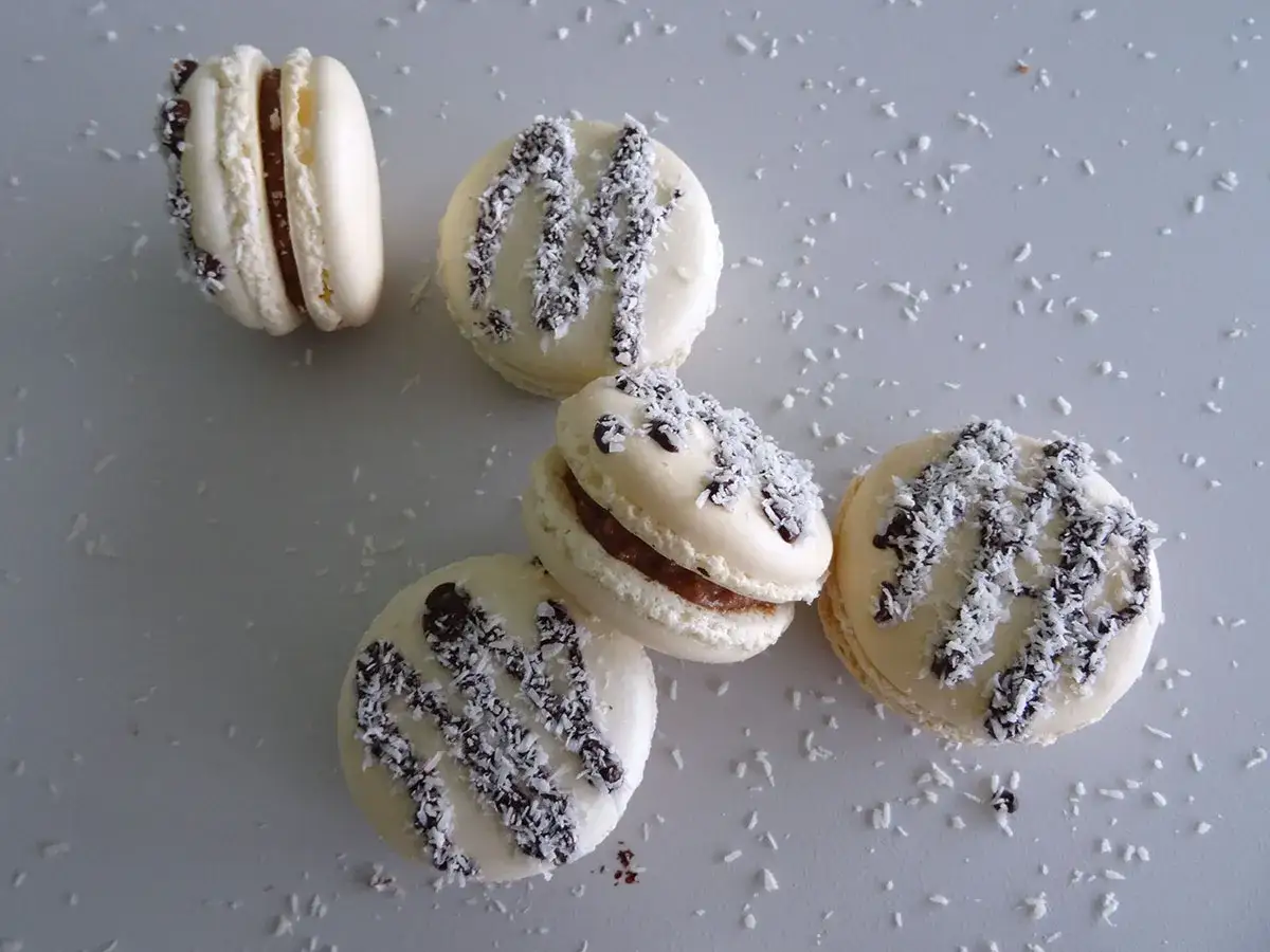 Macarons à la ganache coco, saupoudrés de noix de coco râpée et de copeaux de chocolat noir.