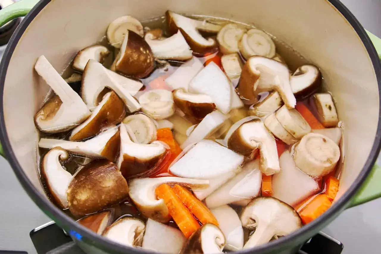 A pot of simmering japanese fish soup, filled with shiitake mushrooms, daikon radish, and carrots.