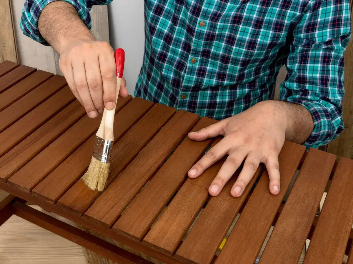 Persona con camisa a cuadros pinta muebles de madera con brocha.