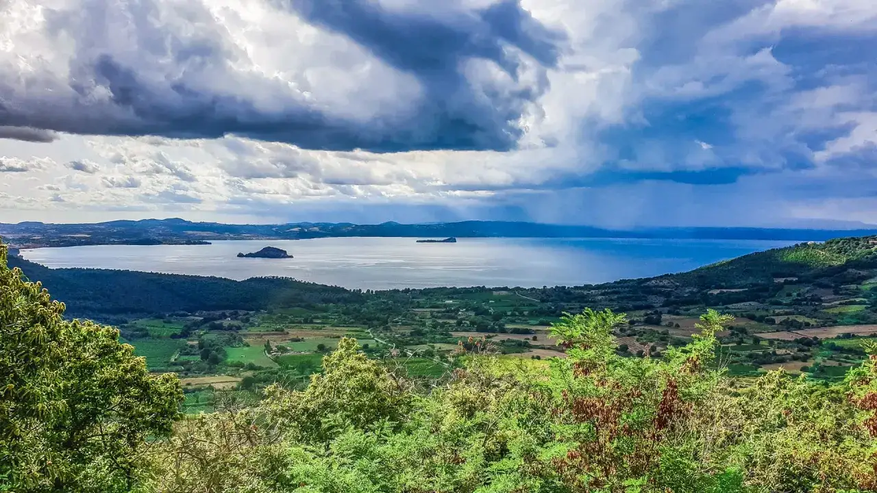 Paesaggio lacustre con isole e colline verdi, ideale per scoprire paesi da vedere vicino Roma. Nuvole drammatiche sul cielo.