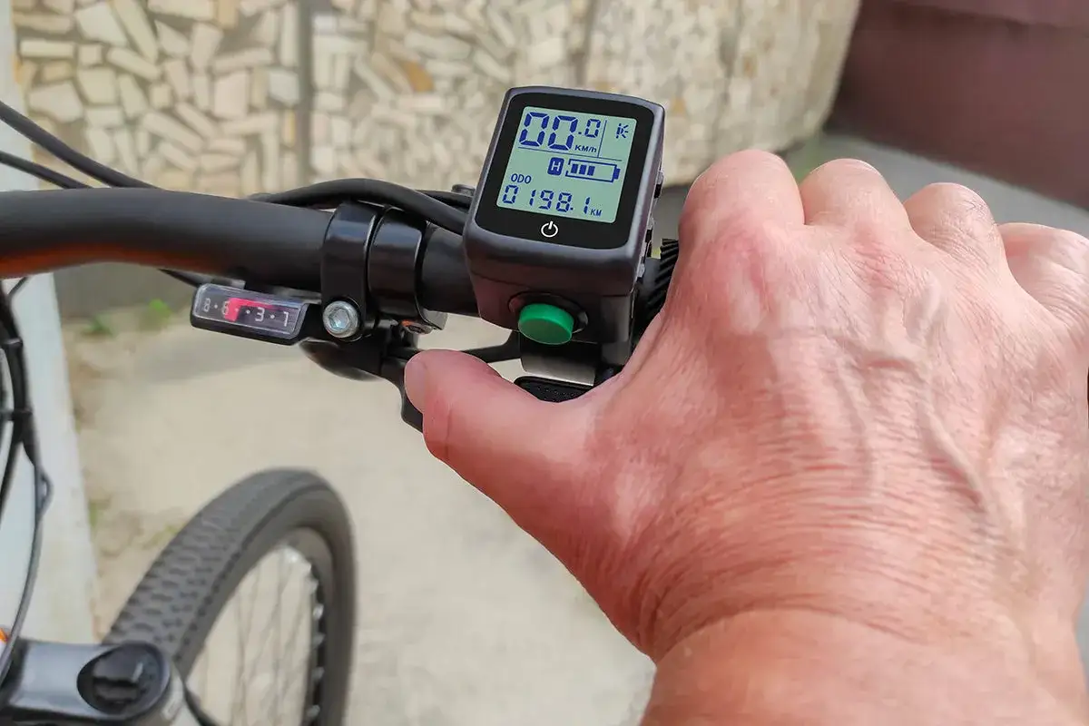 Hand op het stuur van een elektrische fiets zonder trappen. Het display toont 00.0 km/u en 198.1 km.