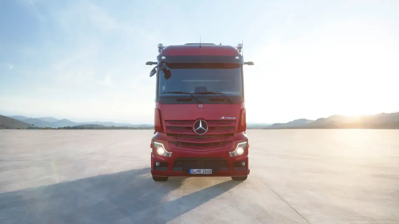 Czerwony Mercedes Actros MP4 na pustkowiu, z górami w tle i zachodzącym słońcem.