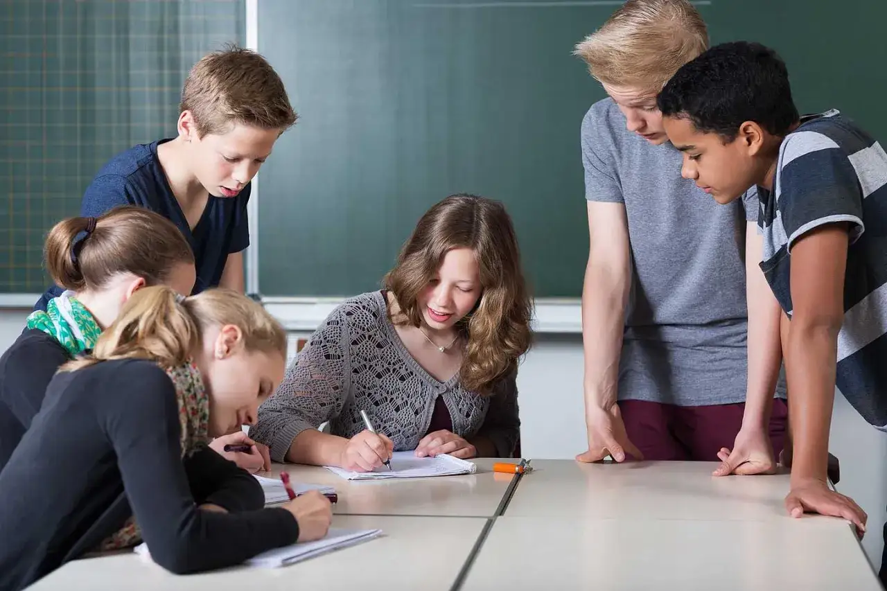 Sechs Schüler, etwa 12 Jahre alt, arbeiten konzentriert an ihren Heften. Ein Junge lehnt sich über den Tisch, um besser zu sehen.