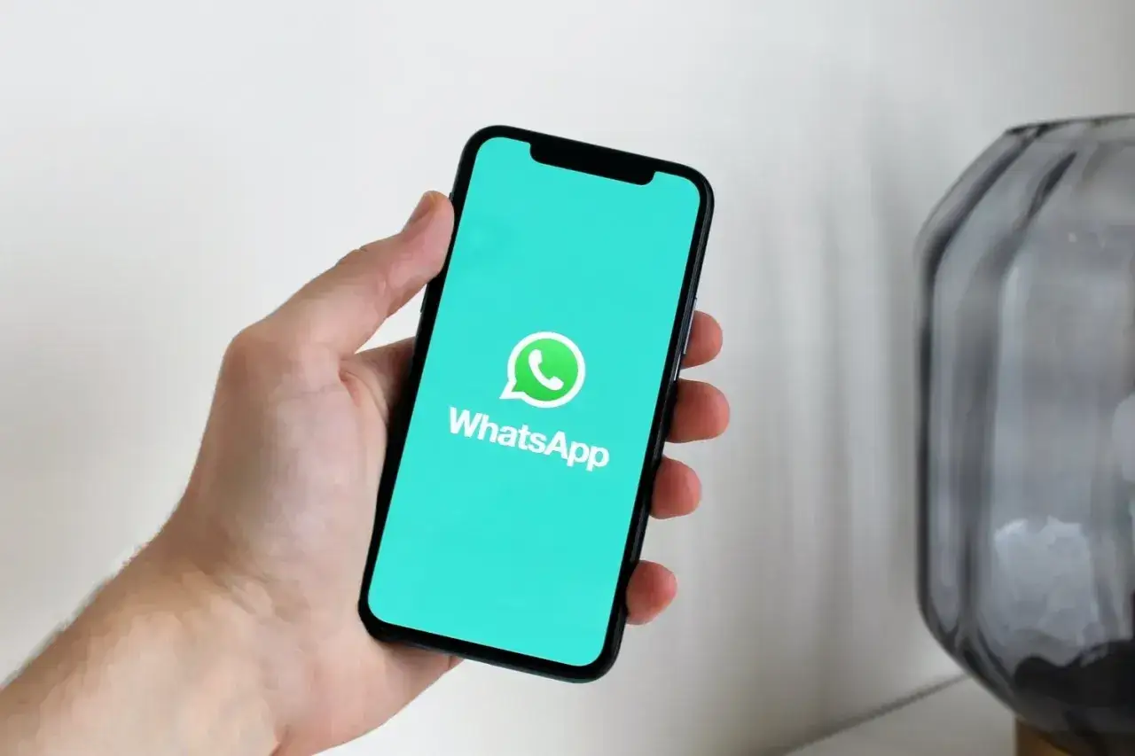 Dłoń trzyma smartfon z zielonym ekranem i logo WhatsApp. Aplikacja istnieje od 2009 roku, łącząc ludzi na całym świecie.