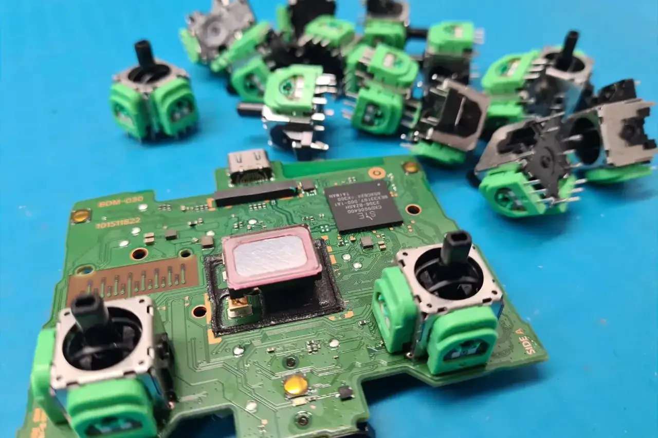 Naprawa DualSense: zielone moduły joysticków i płyta główna kontrolera na niebieskim tle.