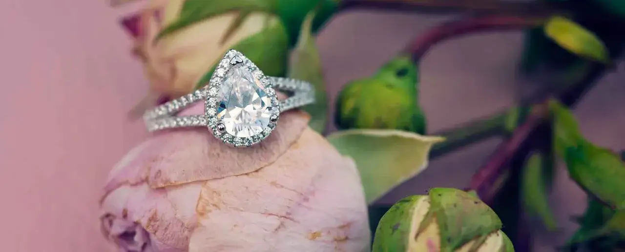 Anello a goccia scintillante su un fiore rosa, simbolo di amore eterno e purezza.
