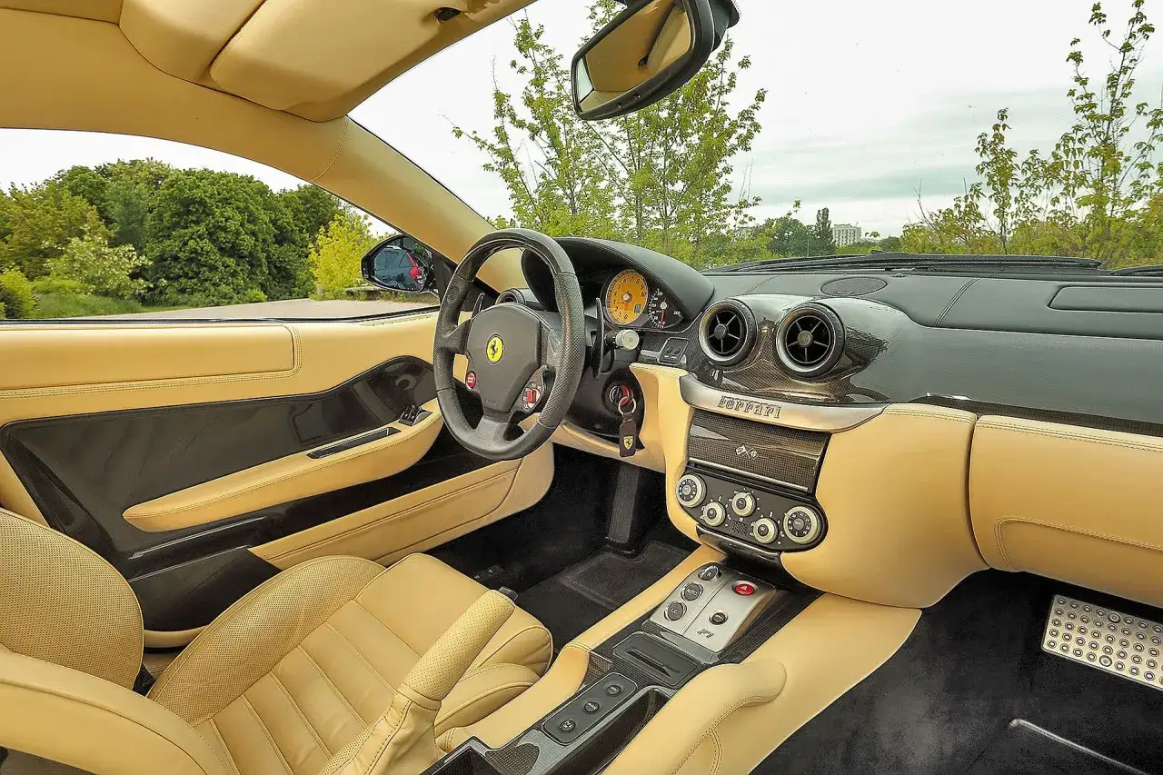 Wnętrze Ferrari 599 z beżową skórzaną tapicerką, karbonowymi detalami i sportową kierownicą.