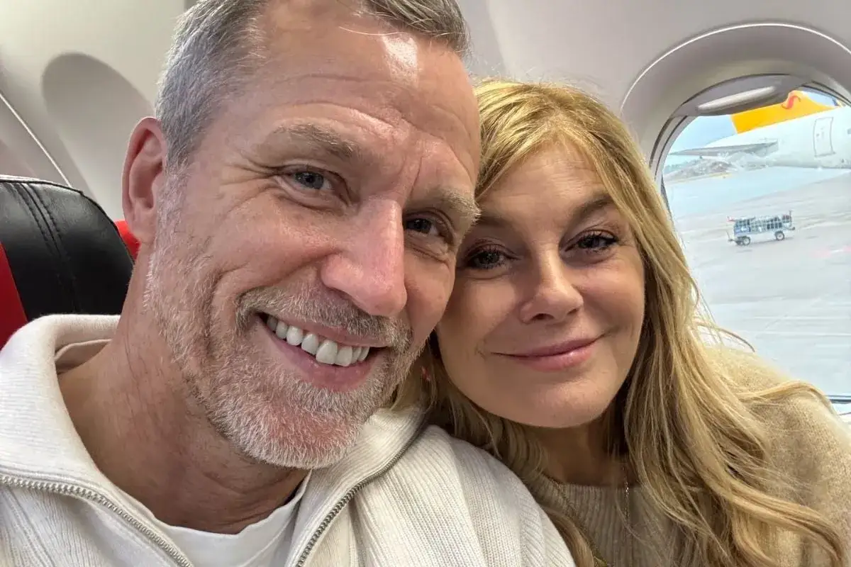 Pernilla Wahlgren och hennes partner ler mot kameran ombord på ett flygplan.