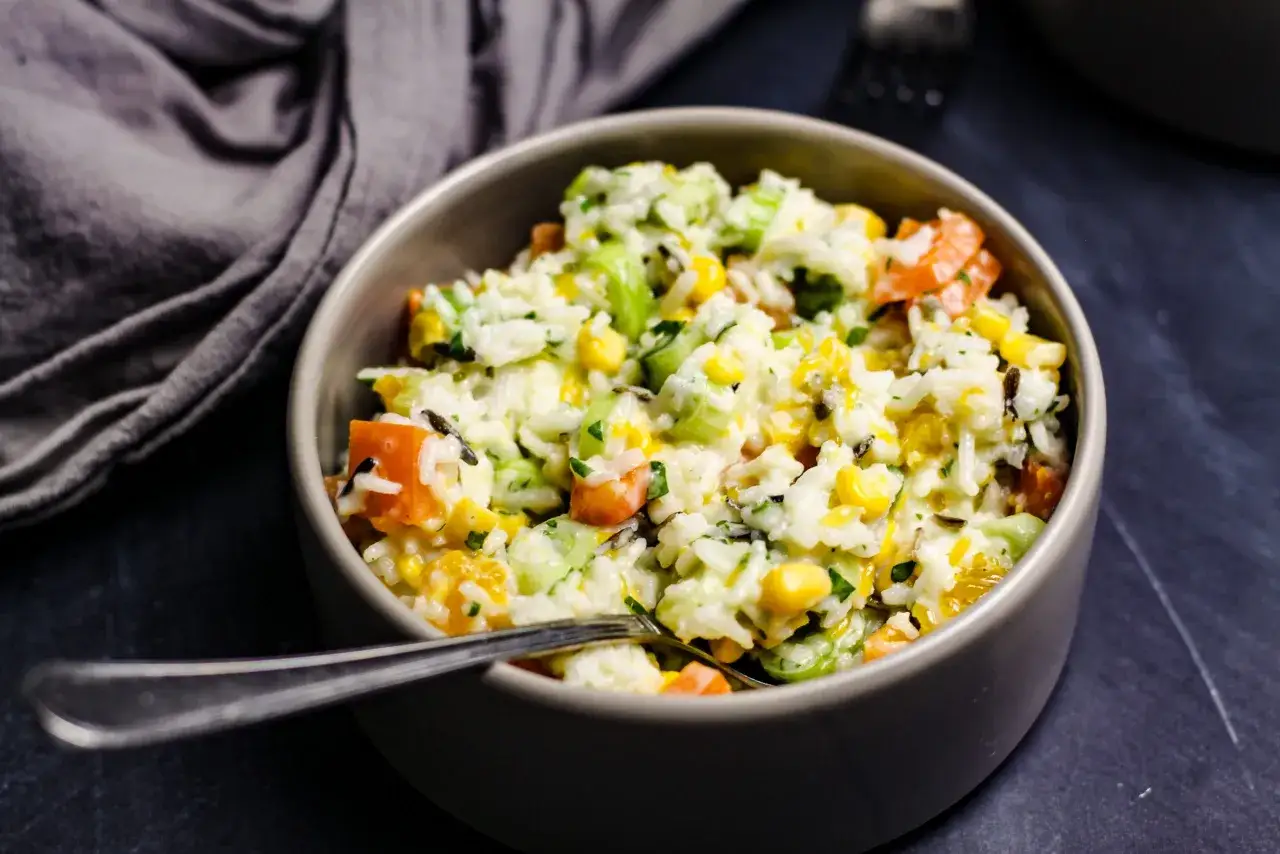 Reissalat mit Mandarinen, Mais und Sellerie, serviert in einer grauen Sch&uuml;ssel mit einer Gabel.