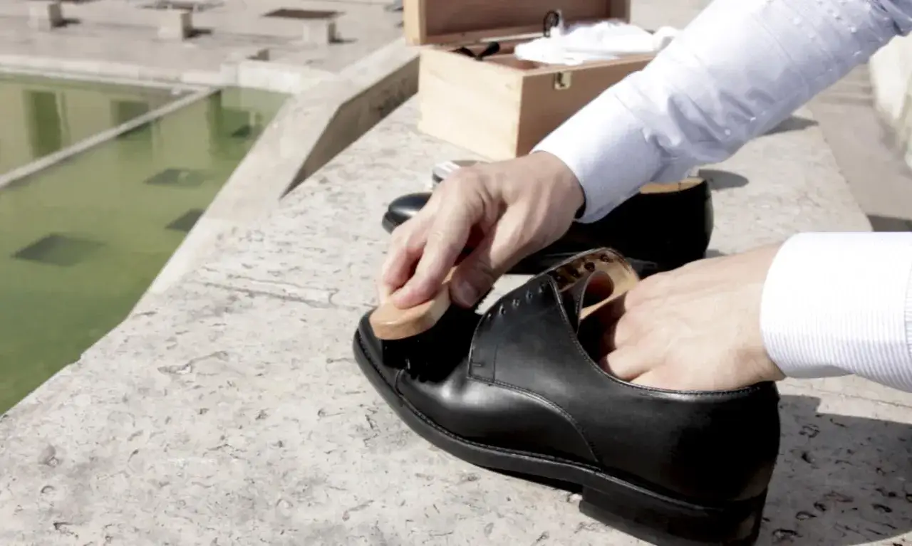 Un homme utilise une brosse pour lustrer une chaussure en cuir noir, une m&eacute;thode pour comment enlever du cirage sur des chaussures en cuir.