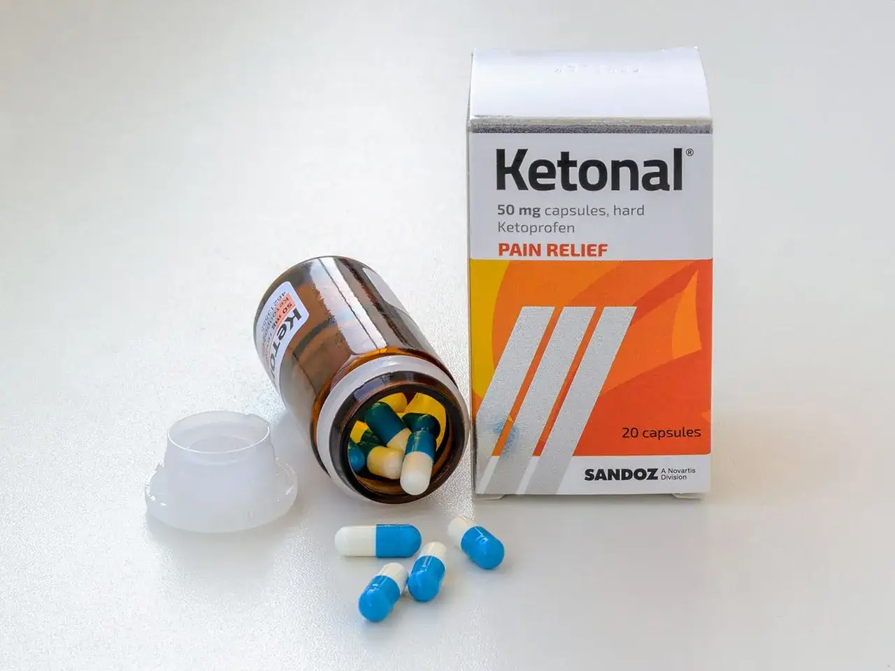 Ketonal w tabletkach, lek przeciwbólowy. Kilka kapsułek leży obok otwartego opakowania i buteleczki.