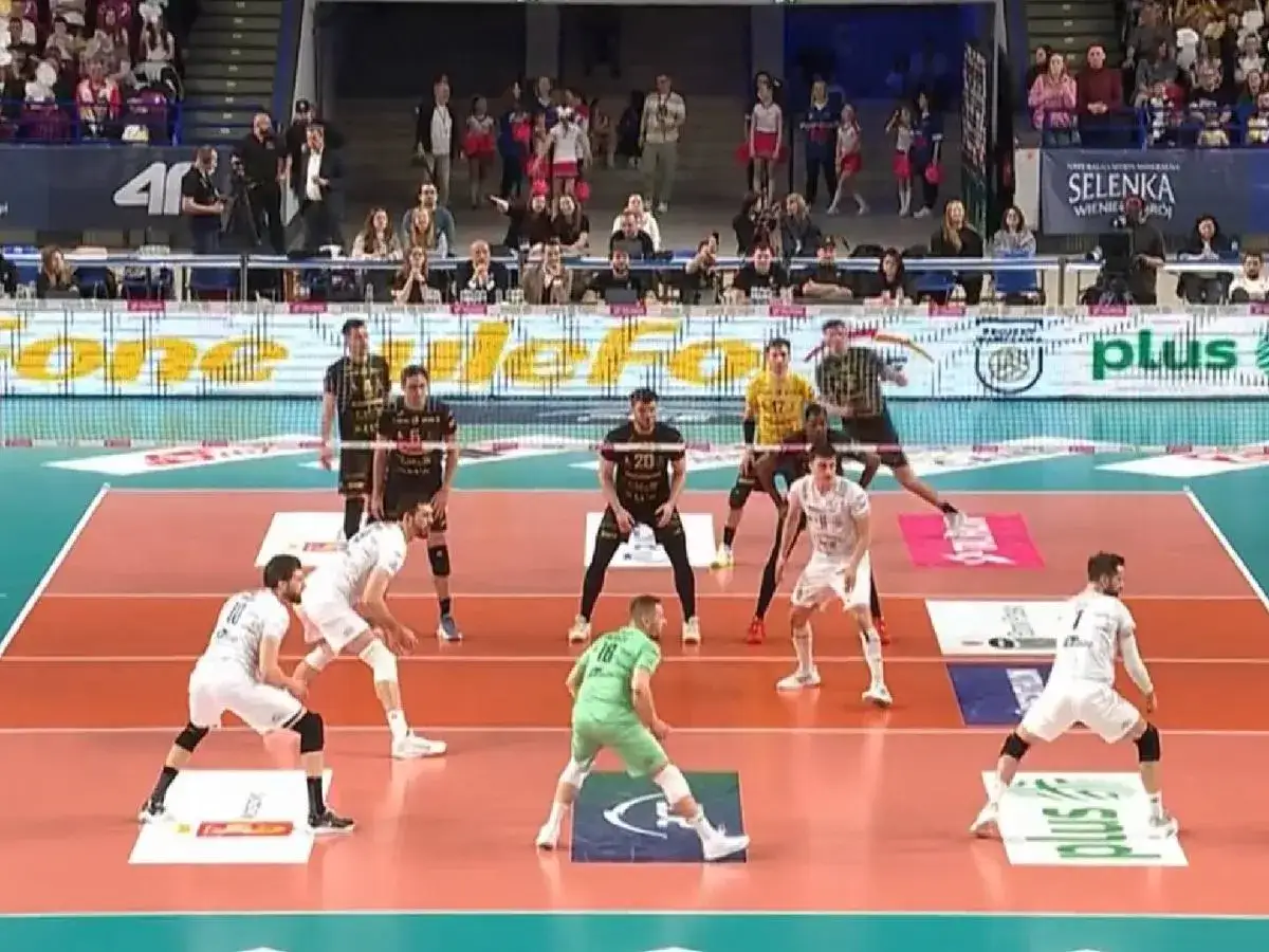 Mecz siatk&oacute;wka mężczyzn plusliga. Zawodnicy w białych i czarnych strojach gotowi do akcji na boisku, publiczność na trybunach.