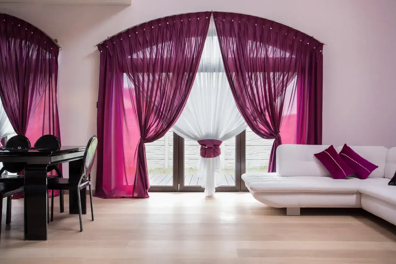 Schiebegardinen kombinieren: Elegante, flie&szlig;ende Stoffe in Lila und Wei&szlig; schaffen ein luxuri&ouml;ses Ambiente vor dem gro&szlig;en Fenster.