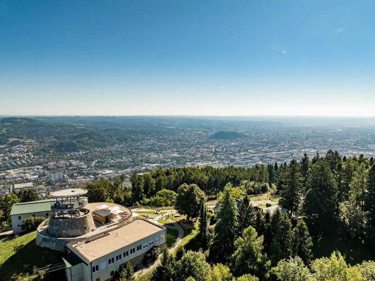 Blick über Graz mit dem Uhrturm in der Ferne. Hier finden sich einige der schönsten graz geheimtipps, versteckt zwischen grünen Hügeln und Wäldern.