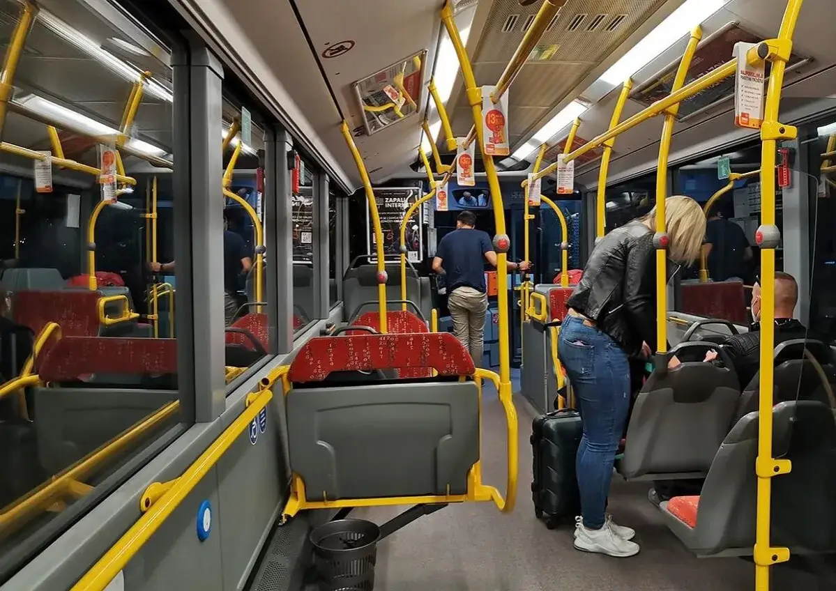 Wnętrze autobusu, żółte poręcze, siedzenia, pasażerowie z bagażami. Zadar komunikacja miejska.