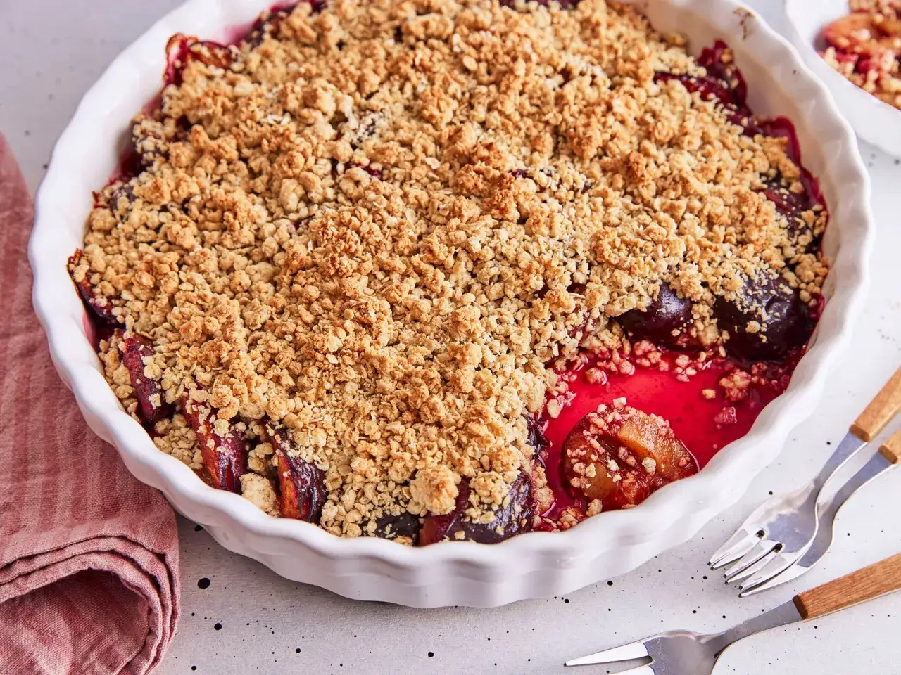 Ein frisch gebackener Zwetschgen Crumble in einer wei&szlig;en Auflaufform. Die goldbraune Streuselhaube bedeckt saftige, dunkle Zwetschgen.