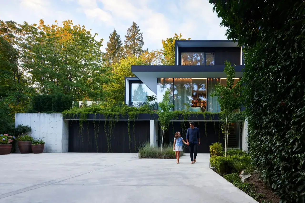 Padre e figlia passeggiano verso la loro casa del futuro, un'elegante villa moderna immersa nel verde.