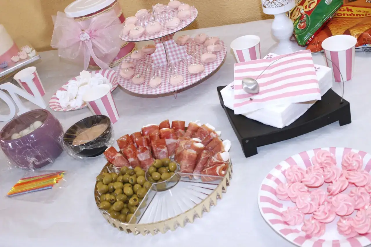 Deliciosa comida para baby shower: jamón serrano, aceitunas, merengues rosas y dulces en bandejas.