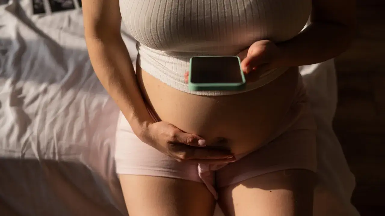 Kobieta trzyma telefon na swoim twardym brzuchu w ciąży.