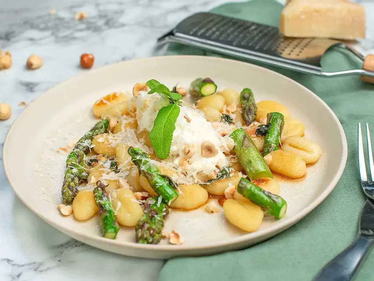 En tallrik med gnocchi, sparris och en klick ricotta, toppad med riven parmesan och nötter. Ett härligt gnocchi recept!