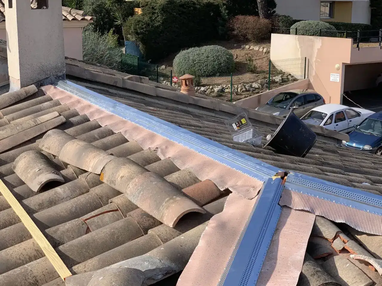 Travaux de r&eacute;paration de toiture en cours, avec des tuiles ab&icirc;m&eacute;es et des mat&eacute;riaux neufs install&eacute;s.
