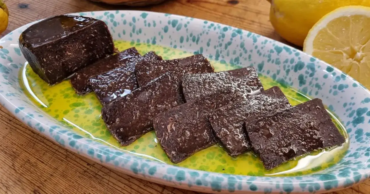 Fette di salame di tonno scuro, lucido e saporito, servite in un piatto con olio e limone.