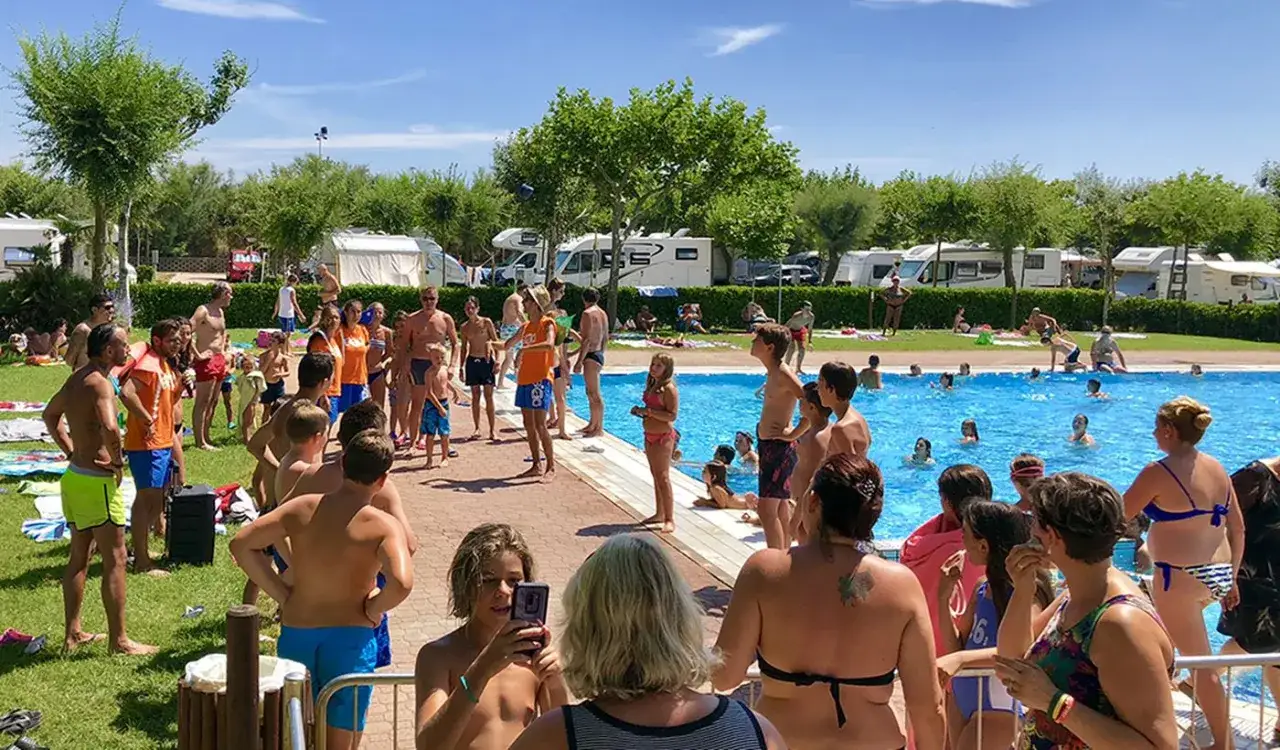 Ludzie odpoczywają i kąpią się w basenie na terenie miramare camping village. Słońce świeci, a niebo jest błękitne.