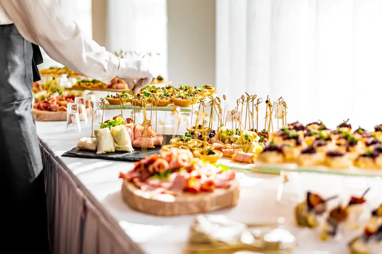 Un serveur en gants blancs ajuste des amuse-bouches sur un buffet. Un d&eacute;licieux repas d'anniversaire est pr&ecirc;t &agrave; &ecirc;tre d&eacute;gust&eacute;.