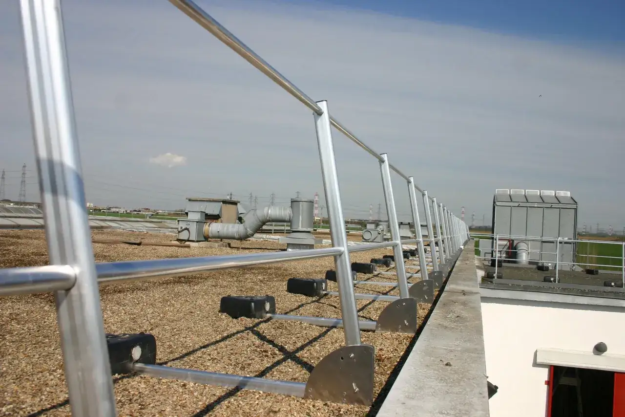 Garde-corps métallique sur une terrasse tropezienne, avec vue sur des installations industrielles et le ciel bleu.