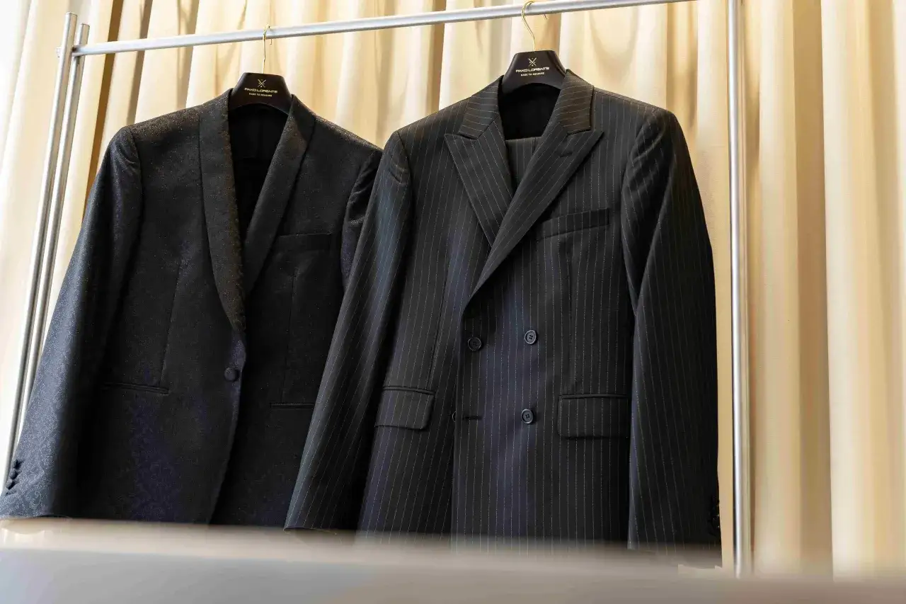 Dwa eleganckie garnitury wiszą na wieszakach. Jeden w prążki, drugi z subtelnym wzorem. Prasowanie garnituru to klucz do nienagannego wyglądu.