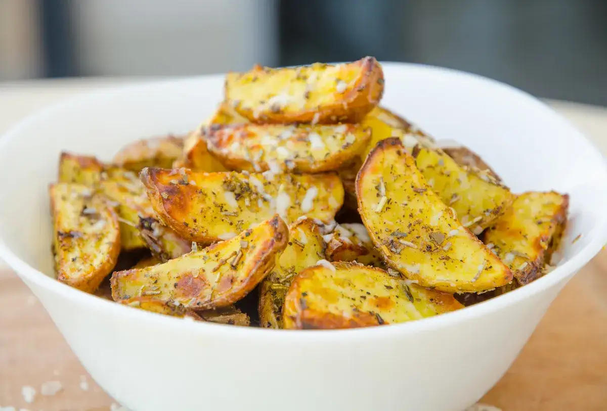 En skål med gyllene klyftpotatis i ugn, kryddad med örter och ost. Perfekt som tillbehör!