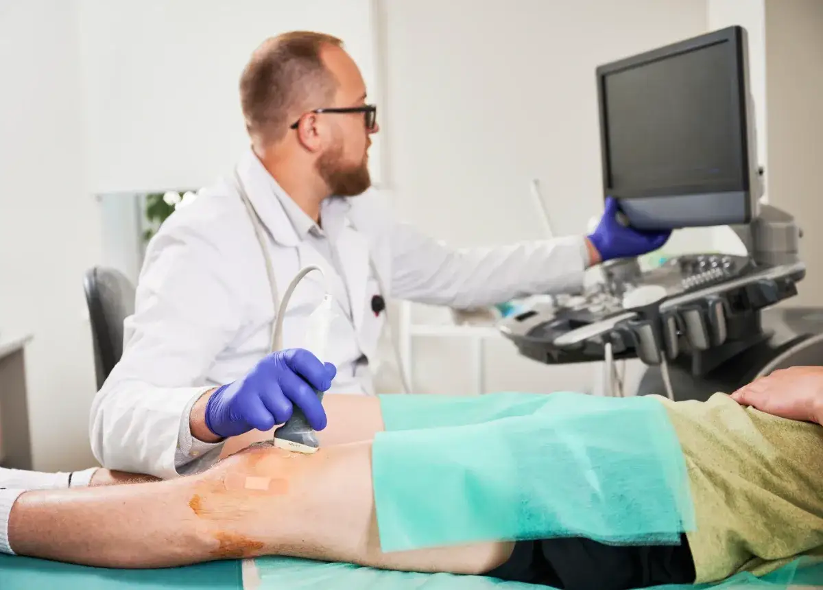 Lekarz wykonuje USG kolana pacjenta, badanie kluczowe dla diagnostyki i planowania leczenia, np. trombolizy.