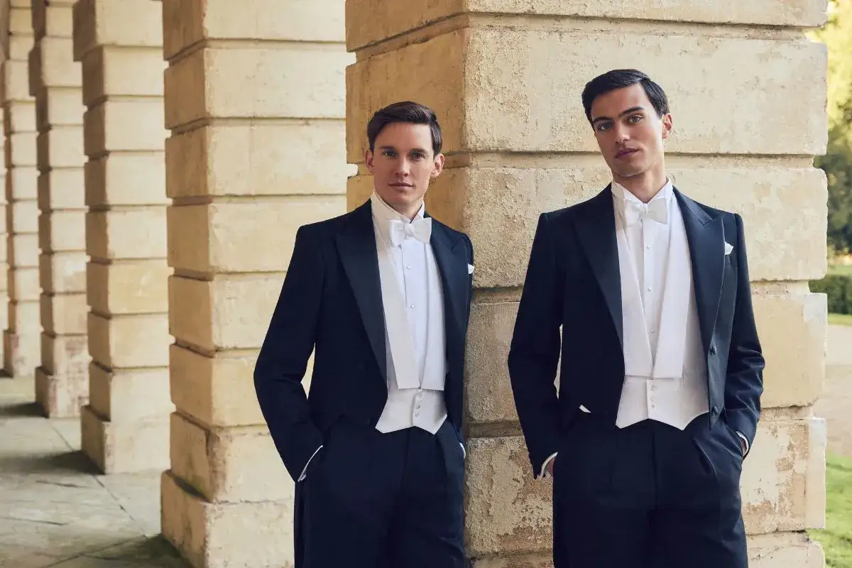 Two men in formal attire demonstrate how to wear a white tie with tailcoats, crisp shirts, and waistcoats.