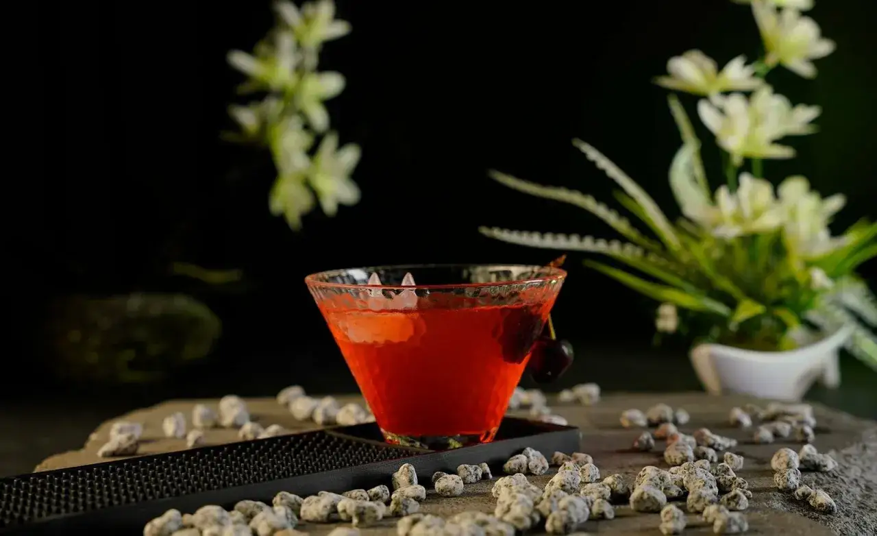 En vackert serverad Singapore Sling med k&ouml;rsb&auml;r, omgiven av stenar och blommor.