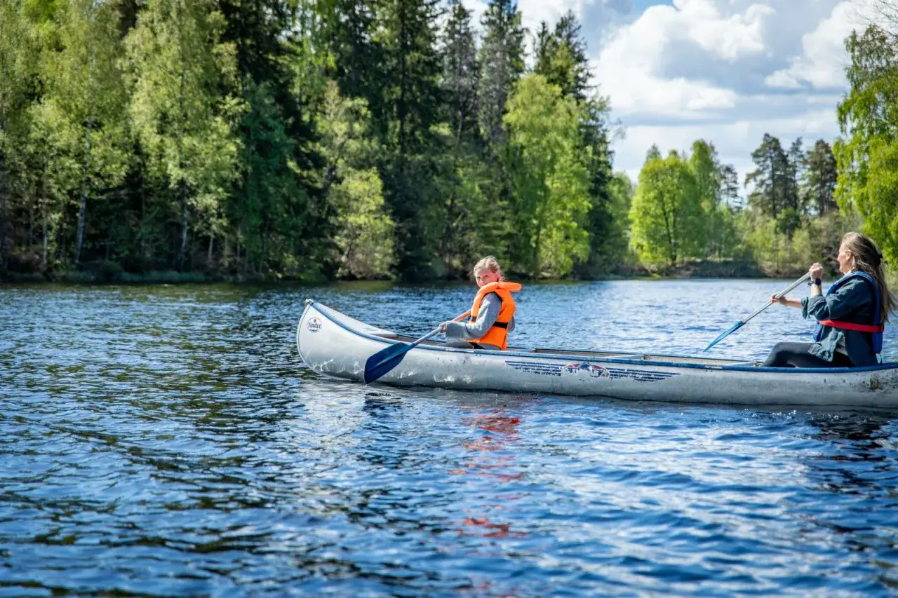 Tv&aring; personer paddlar en kanot p&aring; en sj&ouml;. En flicka med orange flytv&auml;st sitter fram och en kvinna bak. En h&auml;rlig dag f&ouml;r kanot vs kajak i svensk natur.