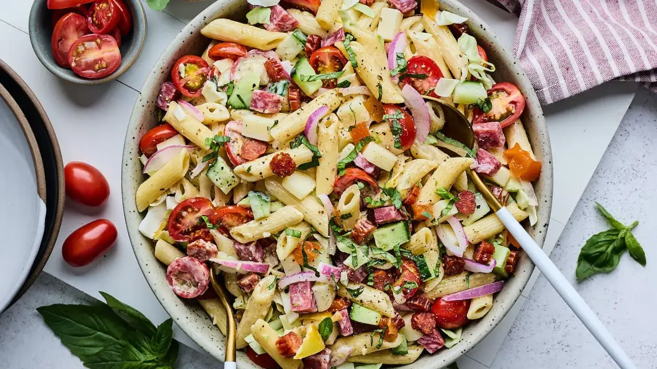 Salade de pâtes froide colorée avec tomates, concombre, salami et oignon rouge, nappée d'une vinaigrette légère. Parfait pour un pique-nique.