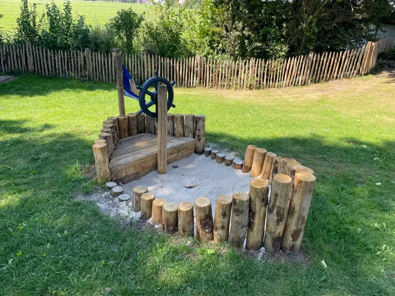 Kreative holzbalken ideen garten: Ein Schiff aus Holzst&auml;mmen mit Sandkasten und Steuerrad l&auml;dt zum Spielen ein.