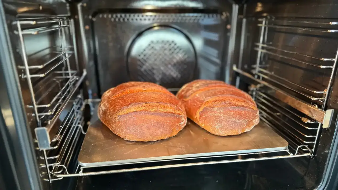 Zwei goldbraune Brote backen auf einem Pizzastein im hei&szlig;en Backofen.