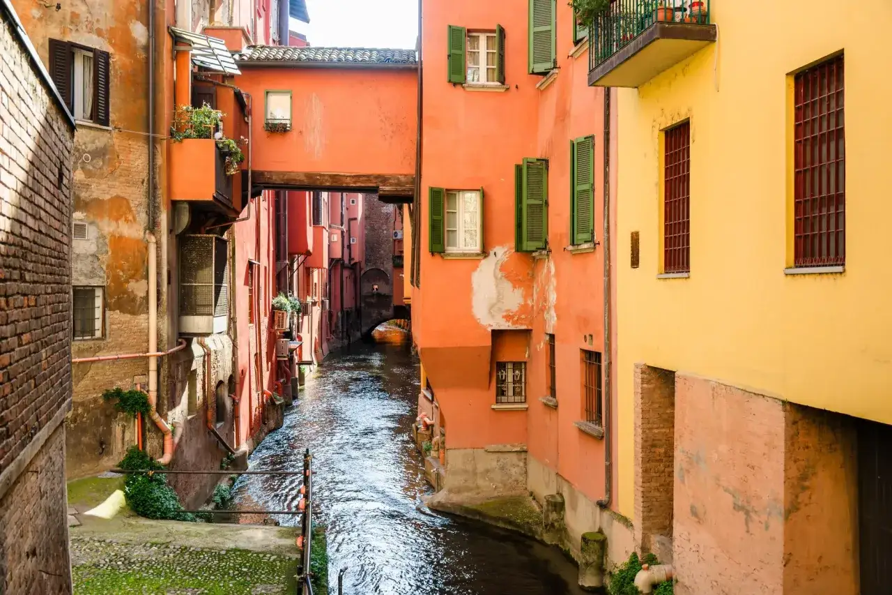 Un canale scorre tra case colorate a Bologna, ricordando i suoi antichi bologna canali sotterranei.