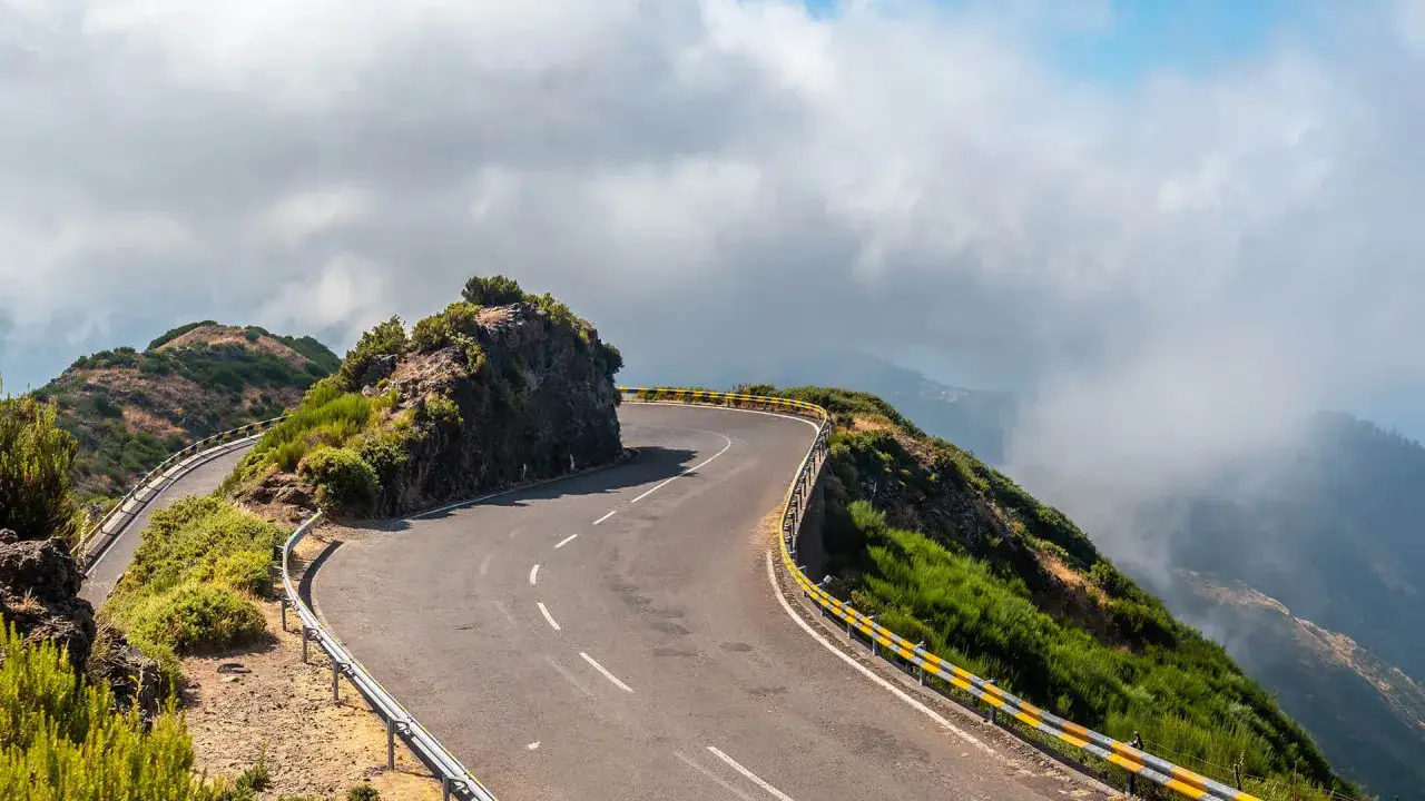 Carretera sinuosa en la **nacional 2 Portugal**, rodeada de vegetaci&oacute;n y acantilados, con nubes que se ciernen sobre las monta&ntilde;as.