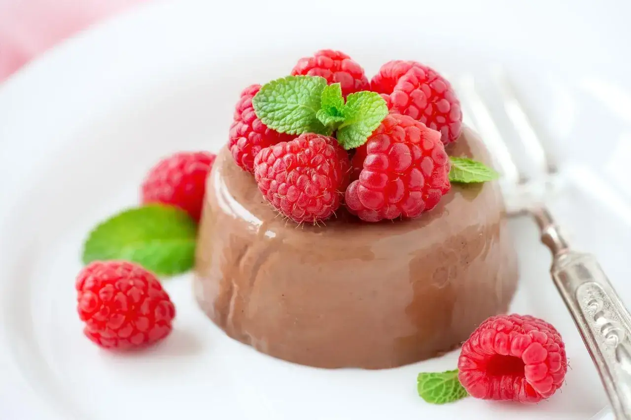 Panna cotta czekoladowa z malinami i miętą na białym talerzu. Wygląda pysznie!