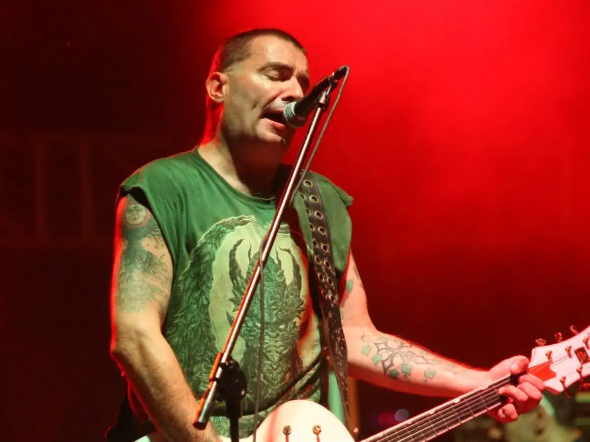 Jeden z członków Kobranocki śpiewa i gra na gitarze na tle czerwonego światła.