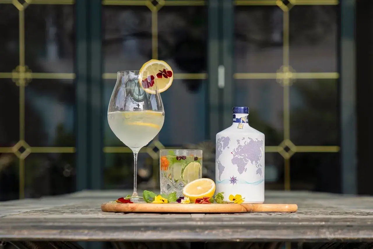Jak zrobić infuzję wódki owocami sezonowymi w 24 godziny? Na stole drink z cytryną i kwiatami, obok butelka wódki z mapą świata.