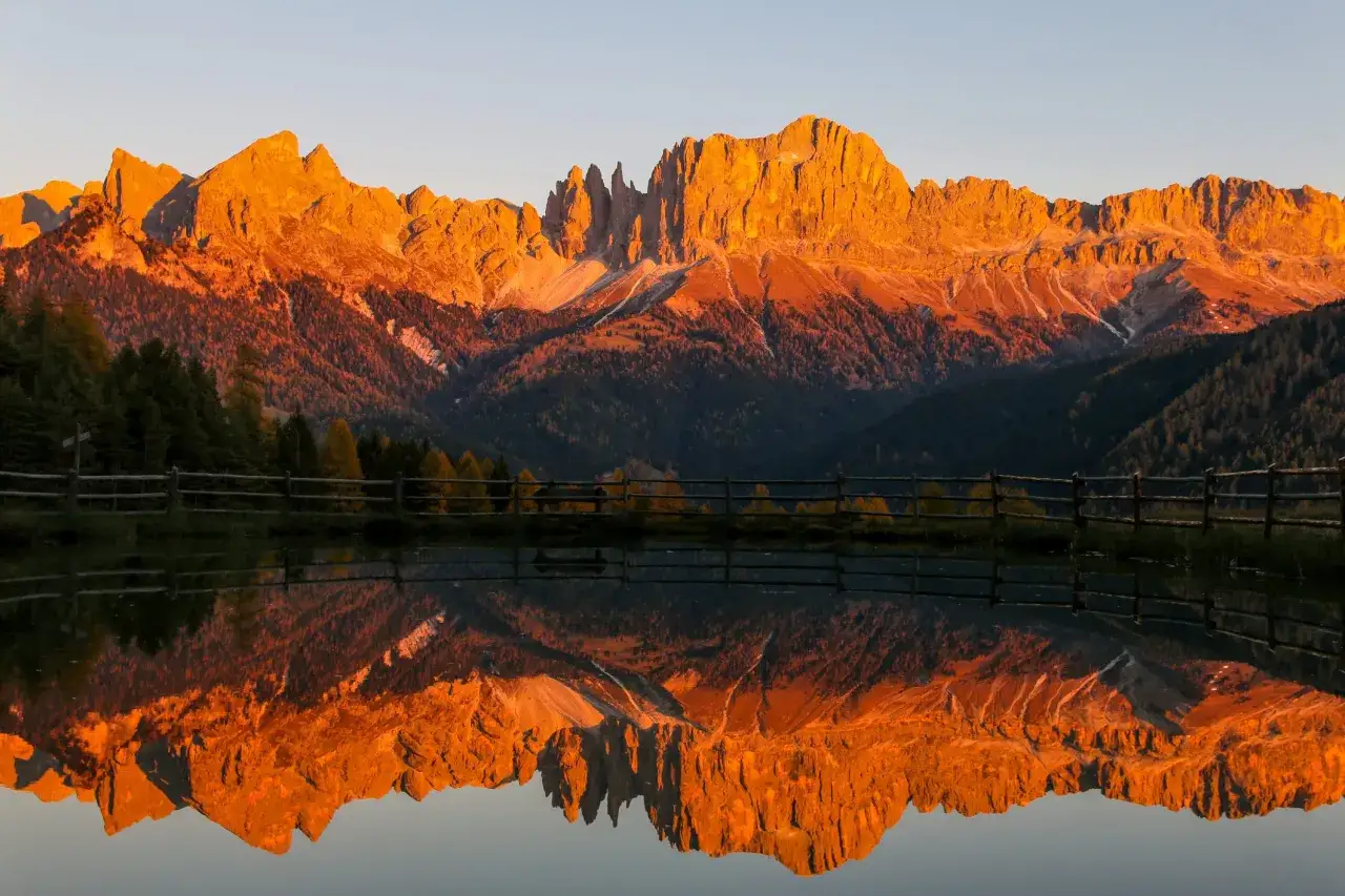 Le **Dolomiti Rosse** illuminate dal tramonto si specchiano in un lago tranquillo, creando un paesaggio mozzafiato.