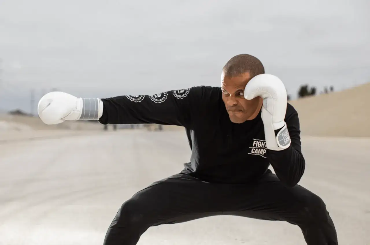 A boxer in a low crouching stance, wearing white gloves and a black 