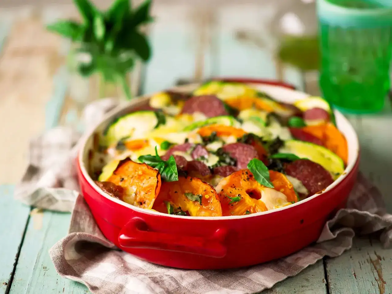 Un plat appétissant de jardinière de légumes, avec des rondelles de courgettes, de tomates et de patates douces, garni de saucisson et de fromage fondant.