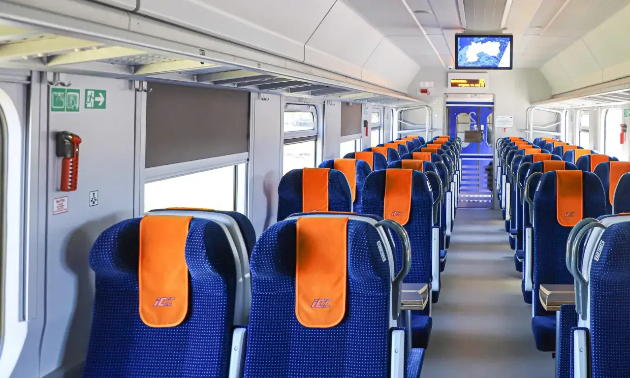 Puste siedzenia w wagonie pierwszej klasy w pociągu. Niebieskie fotele z pomarańczowymi zagłówkami z logo PKP Intercity.